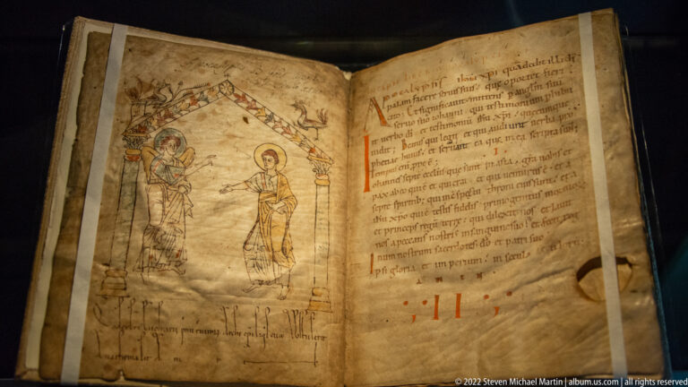 Open medieval manuscript with a line-drawn sacred scene beneath an architectural canopy and Latin text on the facing page.