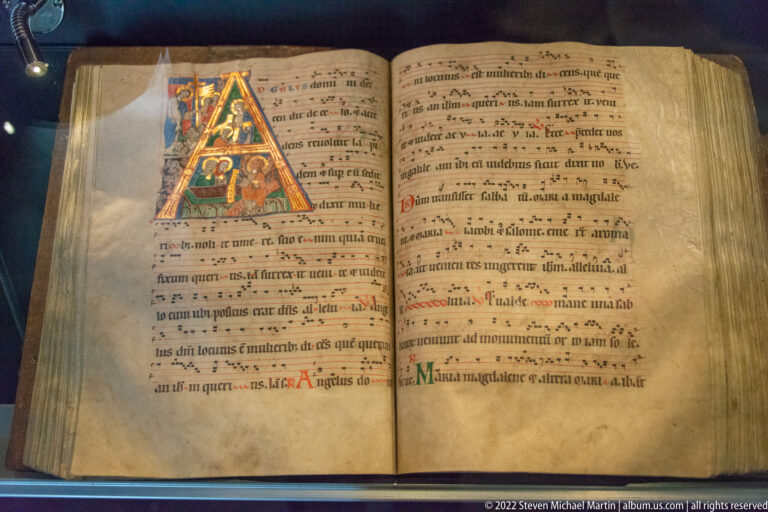 Open liturgical manuscript with a large decorated initial, Latin text, colored initials, and chant or musical notation.