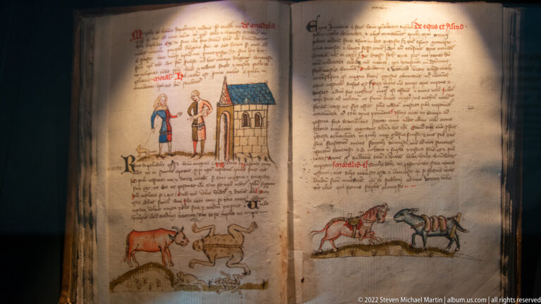 Medieval manuscript pages with drawings of two people by a small building, cattle, and mounted riders among dense handwritten text.