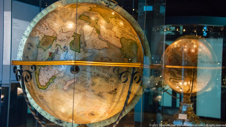 Two historic terrestrial globes in glass cases, with painted maps, coordinate lines, and decorative horizon rings.
