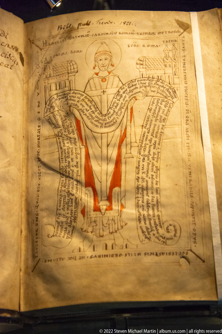 Manuscript page with enthroned clerical figure, red-accented robes, architectural forms, and curling bands of handwritten text.
