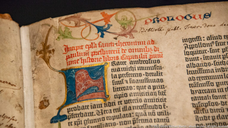 Latin manuscript page with a large blue, red, and green decorated initial, red rubrication, and later marginal notes.
