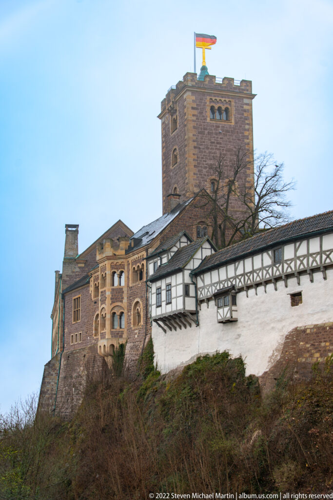 Wartburg keep rising above connected stone, plastered, and half-timbered castle buildings on a steep slope.