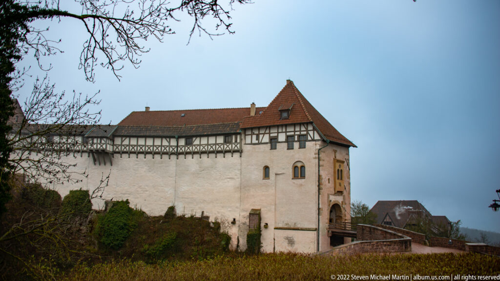 Long white castle wall with upper half-timbering leading toward a projecting gatehouse at Wartburg.