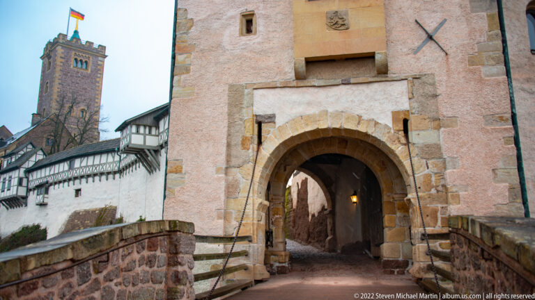 Close view of a round-arched Wartburg gate passage with stone surround, small windows, and heraldic detail above.