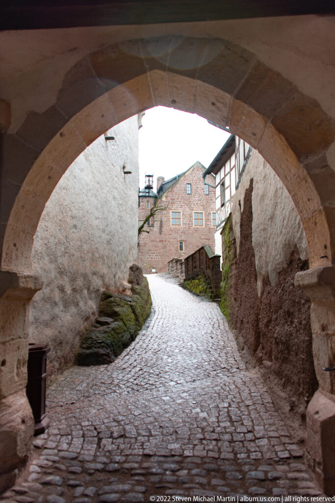 Cobblestone lane passing beneath a broad stone arch between rough plastered and masonry walls at Wartburg.