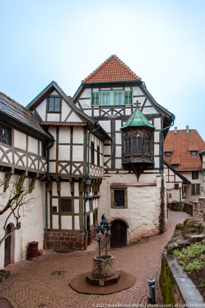 Brick-paved Wartburg courtyard enclosed by half-timbered buildings, with a projecting polygonal bay window.