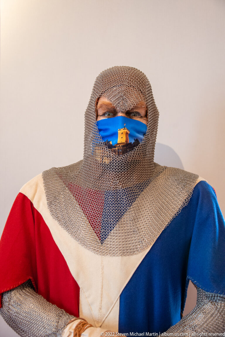 Person wearing chainmail over the head and shoulders with a red, white, and blue medieval-style surcoat.