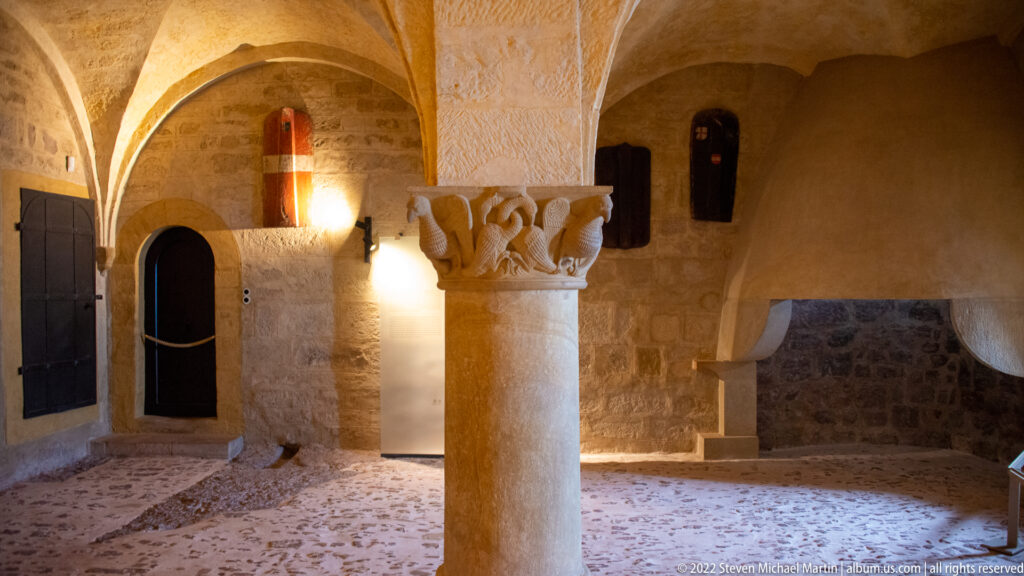 Low stone-vaulted room at Wartburg with central column, carved capital, arched openings, and rough masonry walls.