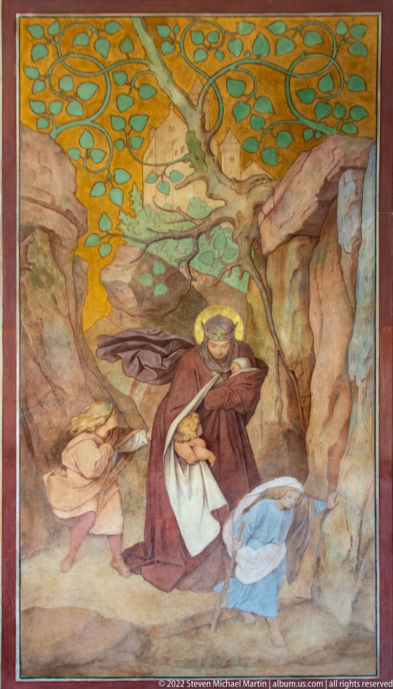 Religious painting of a haloed woman holding an infant in a rocky landscape with another figure nearby.