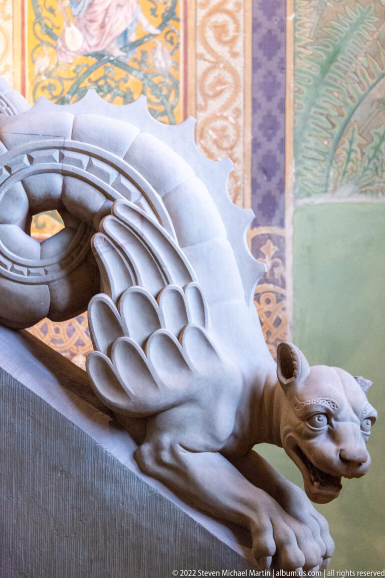 Pale stone winged lion or griffin carving with open mouth and folded feathered wings.