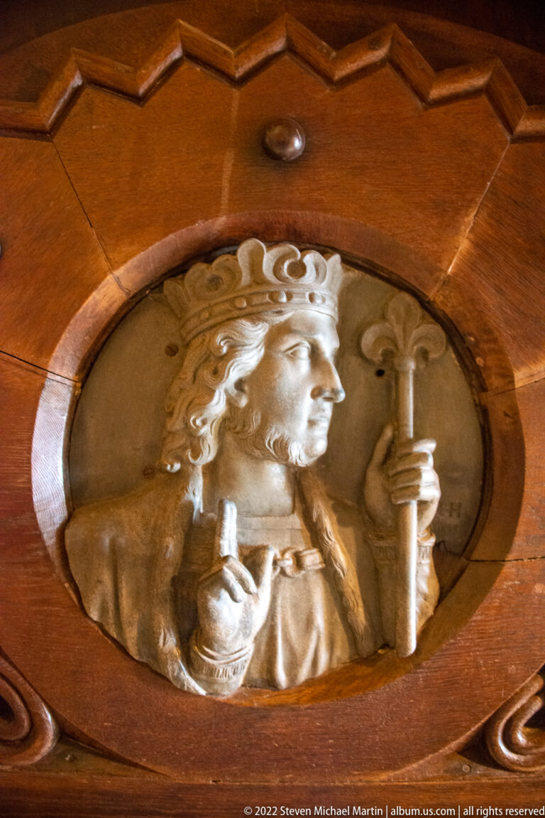 Pale relief medallion of a crowned male ruler holding regalia, set into dark carved wood.