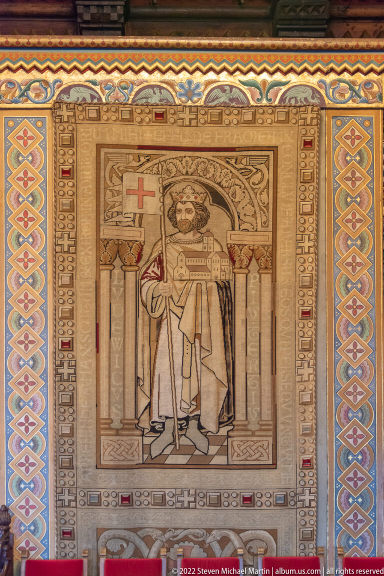 Frontal medieval ruler beneath an architectural canopy, framed by a broad geometric and inscription-like border.