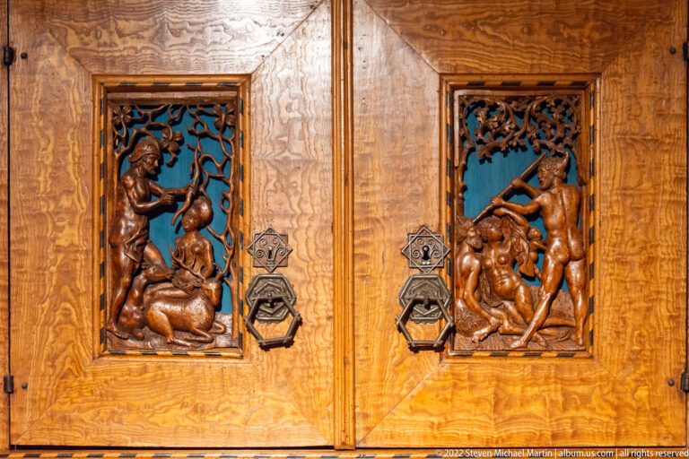 Pair of carved wooden door panels with figural reliefs, pierced foliage, and heavy geometric metal hardware.
