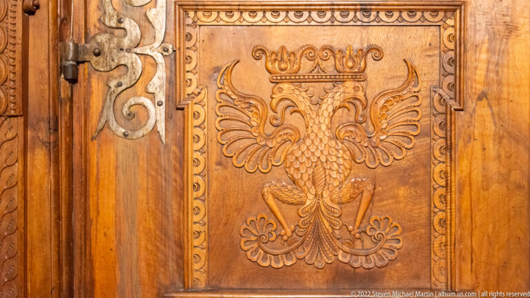 Crowned double-headed eagle carved in relief on a rectangular wooden panel.