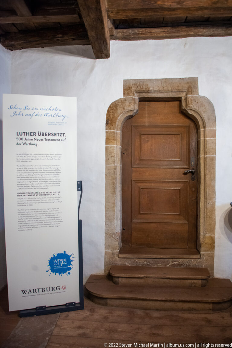 Low wooden door in a rounded stone surround beside a museum panel about Luther's translation work.