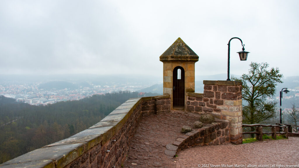 Stone parapet and small roofed lookout niche overlooking a hazy valley and city below Wartburg.