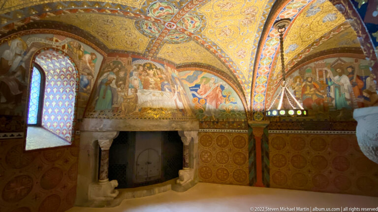 Gold mosaic-covered chamber with narrative scenes, patterned walls, arched window, and stone fireplace.