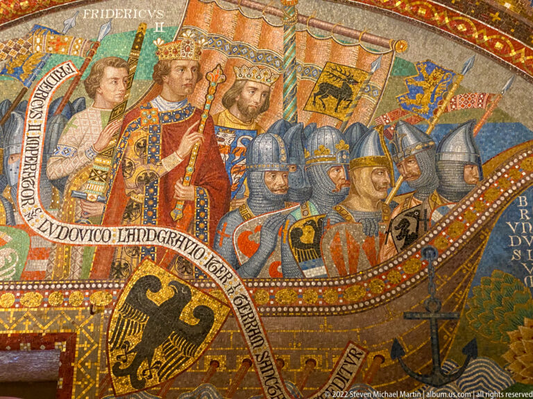 Gold mosaic of a crowned medieval ruler with armored men in a ship beneath heraldic banners.