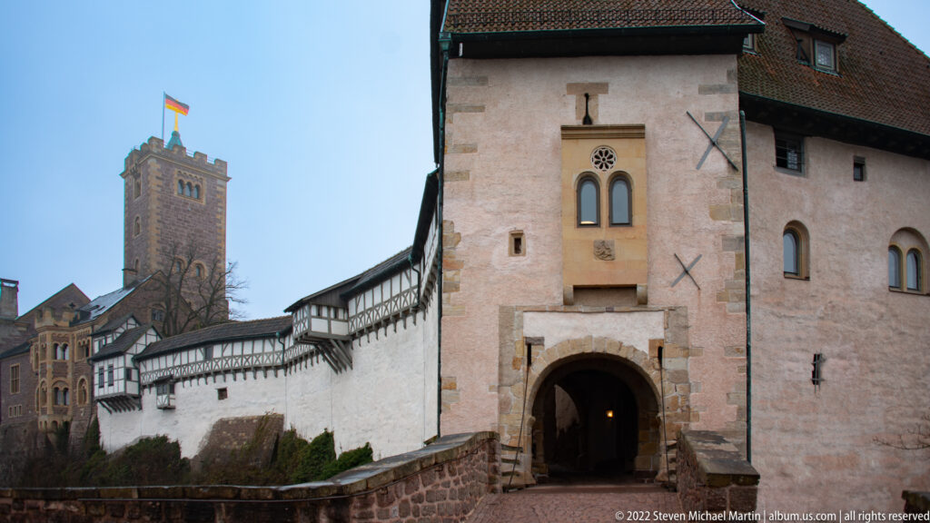 Round-arched Wartburg gatehouse entrance below white walls and half-timbered ranges, with the main tower behind.
