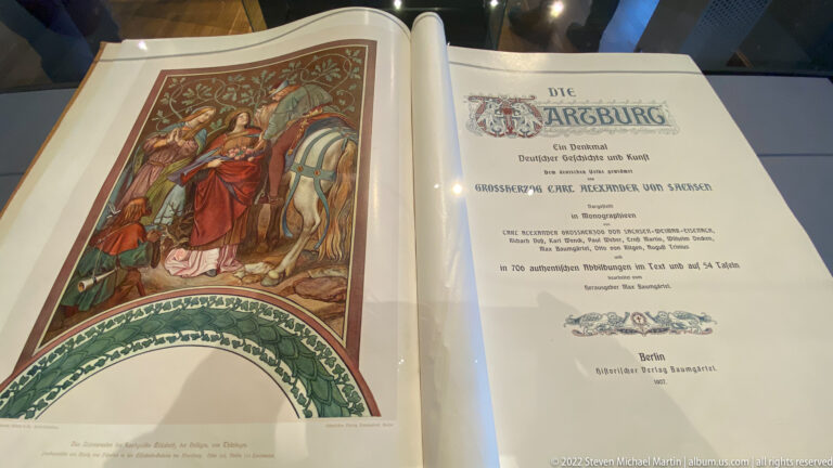 Open historic book with a color illustration on the left and a title page reading 'Die Wartburg' on the right.