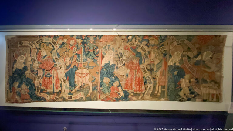 Large historic textile with many richly dressed courtly or religious figures arranged across the full width.
