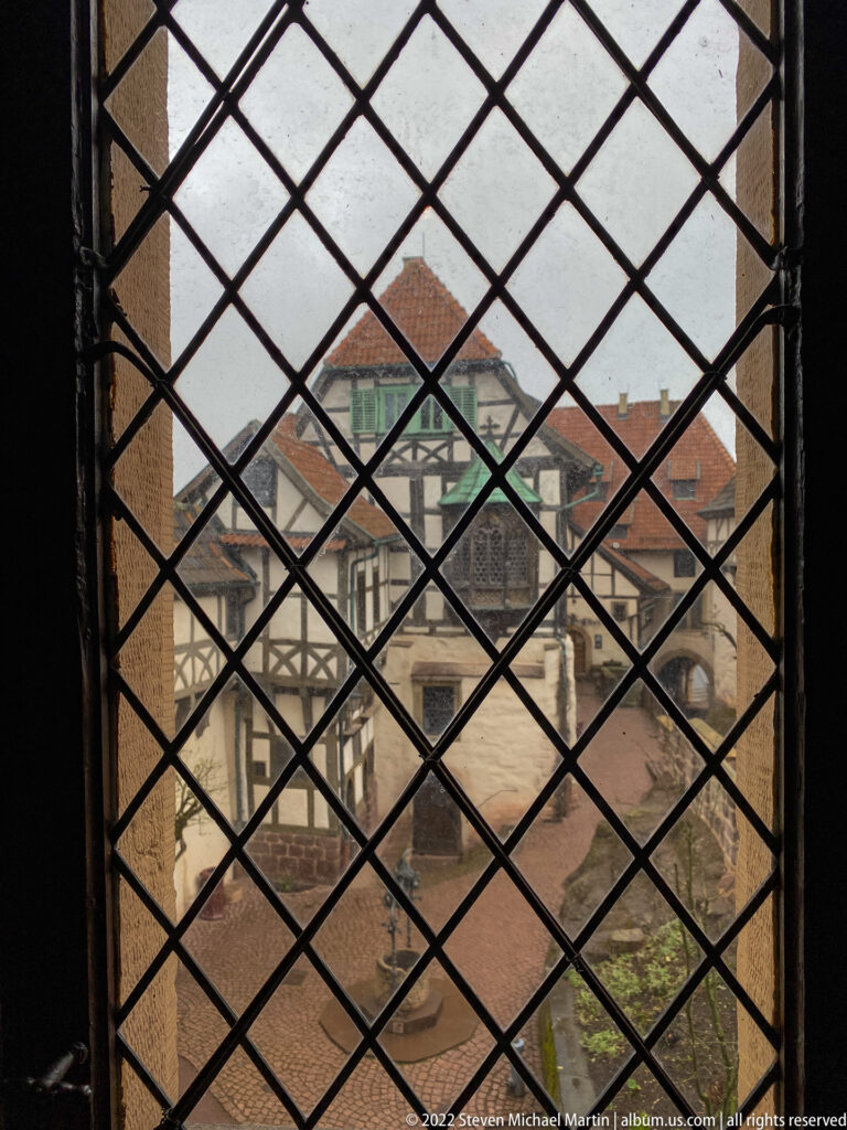 Wartburg courtyard seen through a dark diamond-pattern leaded window lattice.