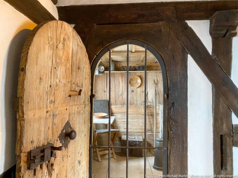 Open heavy plank door in a timber frame with an iron-barred gate immediately beyond.