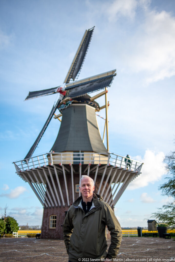 Visitor standing in front of the Keukenhof windmill, with its white gallery and crossing sails filling the background.