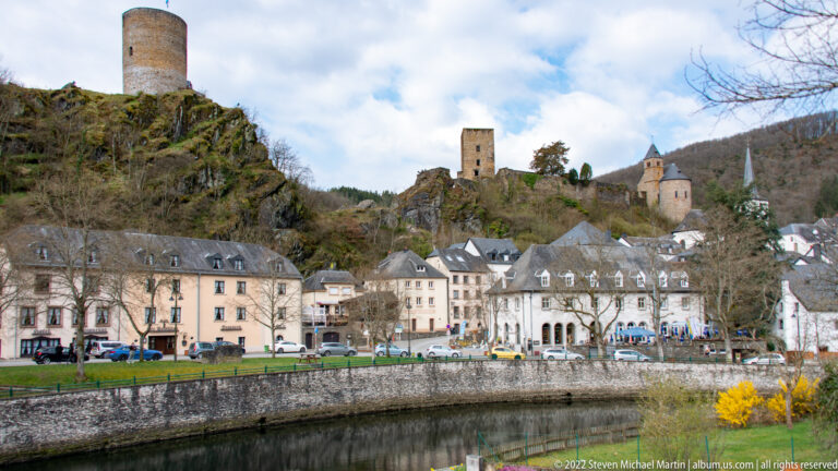 Esch-sur-Sûre riverfront buildings below the castle tower, restored chapel, and parish church spire on the ridge.