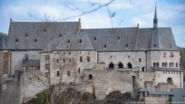 Close view of Vianden Castle's pale stone central range with steep slate roofs, gables, arcaded openings, and lower defenses.