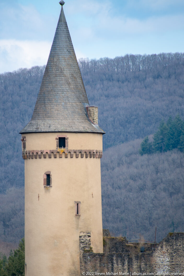 Pale rectangular defensive tower with pyramidal slate roof above a rough stone wall at Vianden Castle.