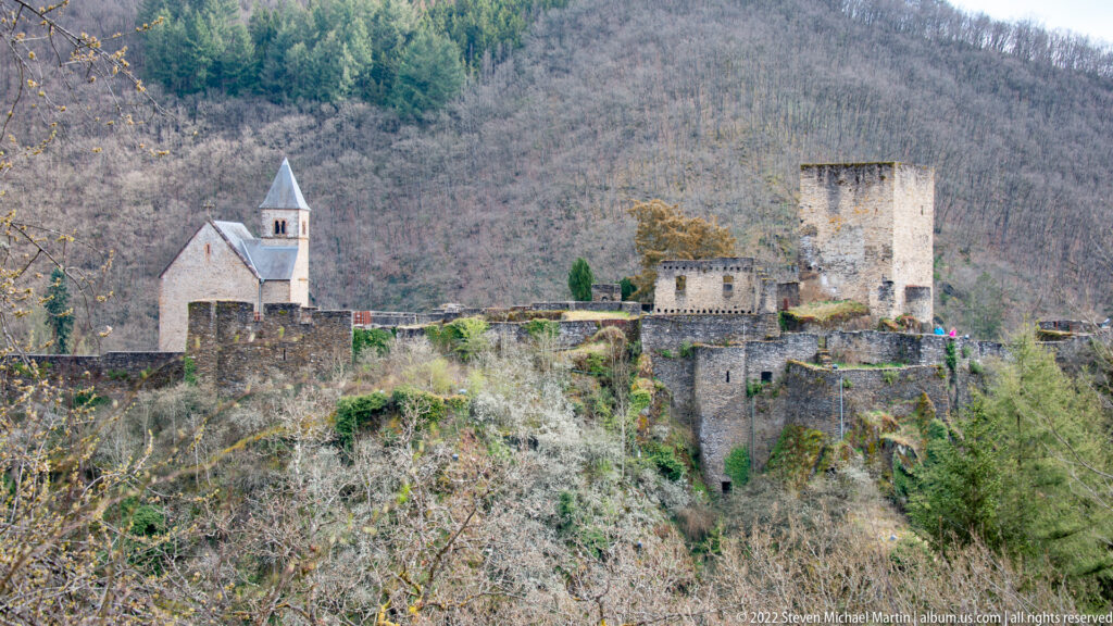 Closer view of Esch-sur-Sûre Castle with chapel, roofless square tower, stone walls, and exposed rock below.