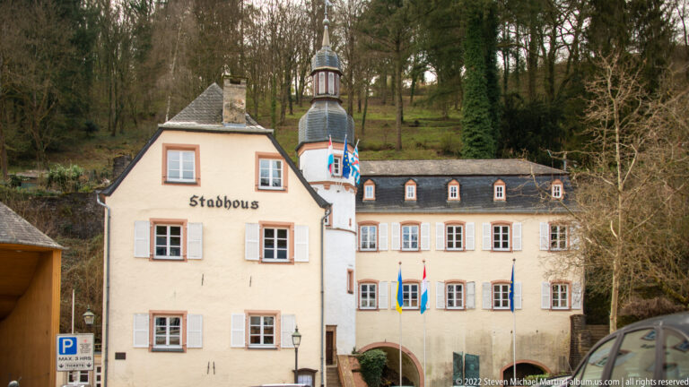Vianden Town Hall marked Stadhous, with shuttered windows, civic flags, and a small tower against a wooded slope.