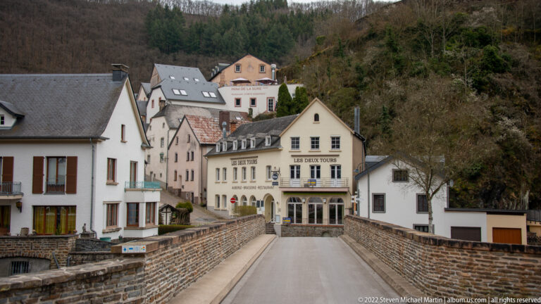 Stone-sided roadway leading toward closely packed village buildings and the signed Hôtel de la Sûre in Esch-sur-Sûre.