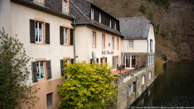 Pale shuttered building with slate roof and terrace built directly along the Sûre in Esch-sur-Sûre.