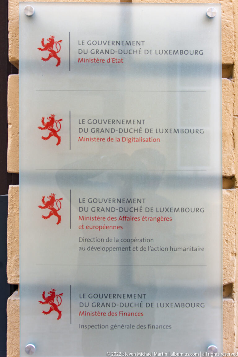 Stacked translucent government plaques with Luxembourg's red lion emblem list several ministries in French.