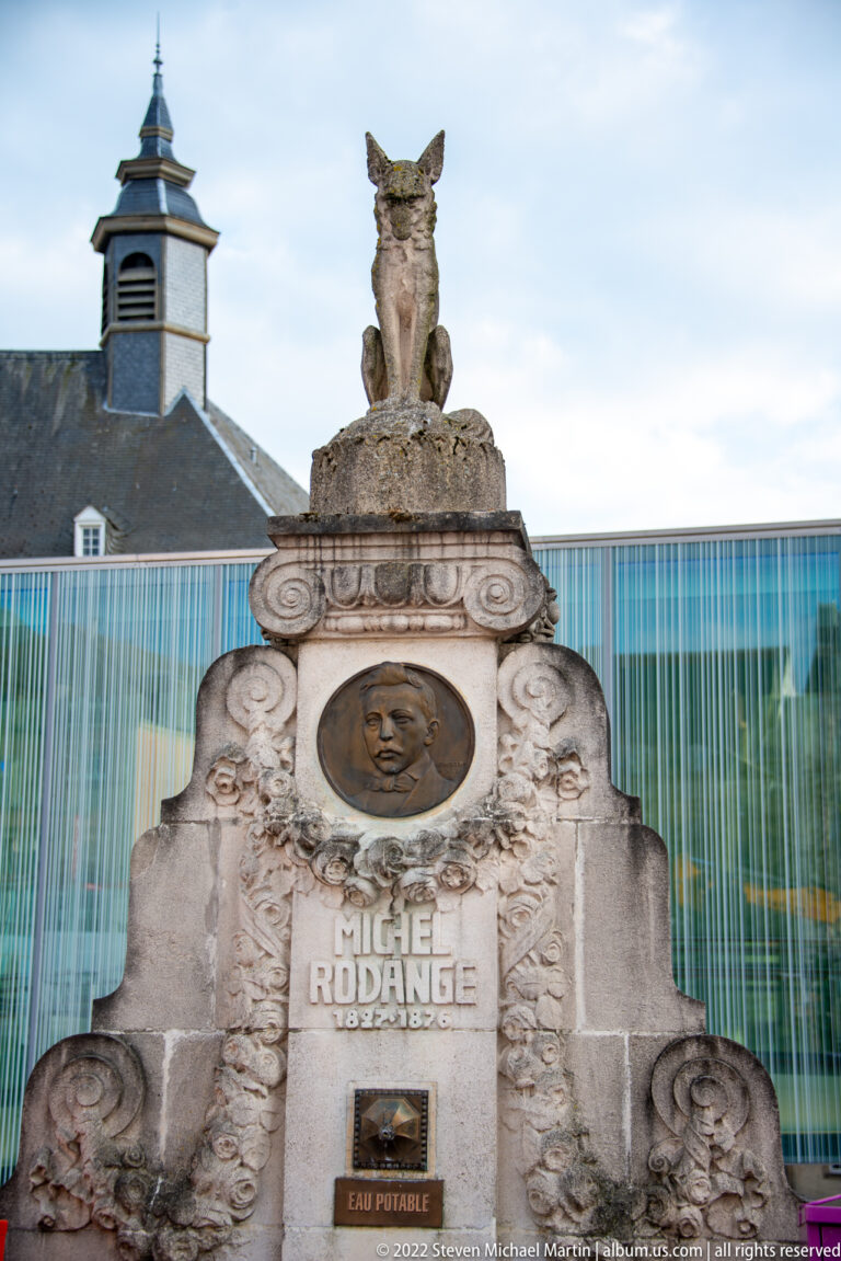 Stone Michel Rodange memorial with portrait medallion, carved name and dates, and a fox sculpture on top.