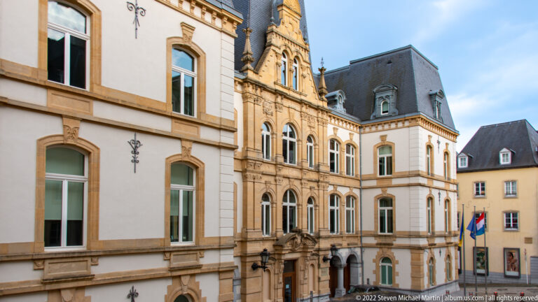 Ornate historic public building with carved stone façade, arched windows, steep slate roof, and official flags.