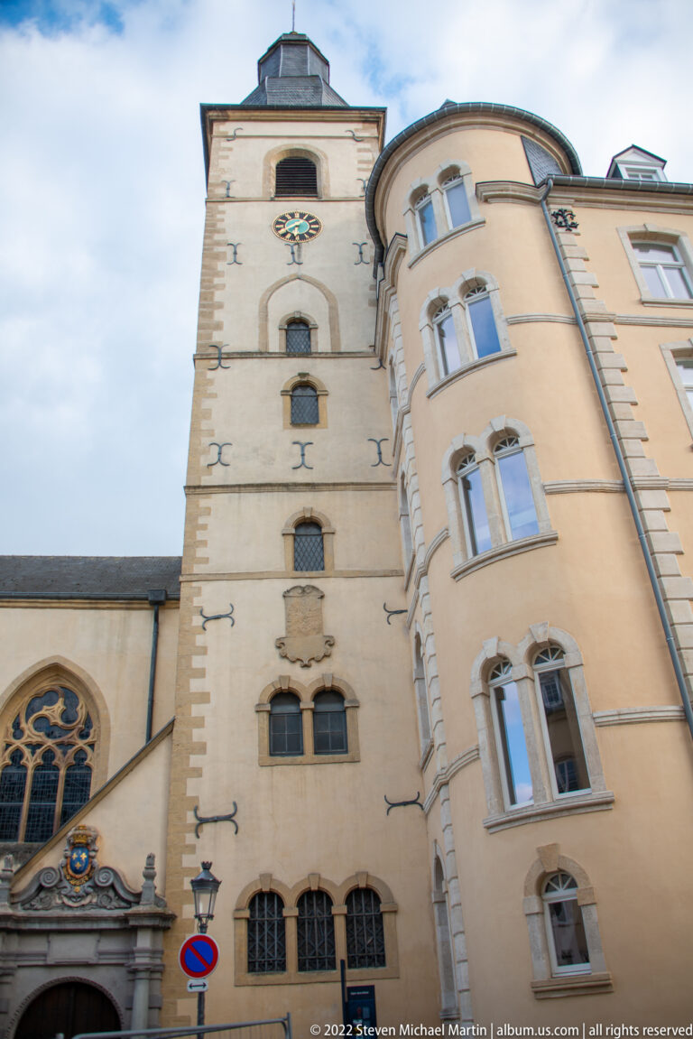 Historic church façade with traceried window beside a tall rounded-corner building with stacked windows.