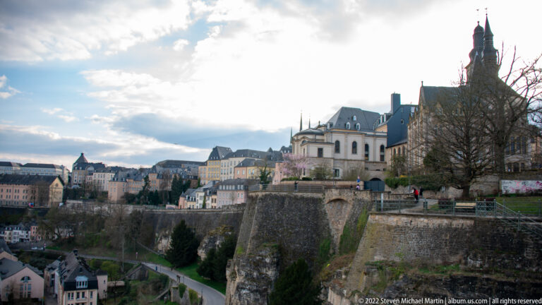 Historic buildings and a tall tower rise above massive stone fortifications overlooking the lower city.