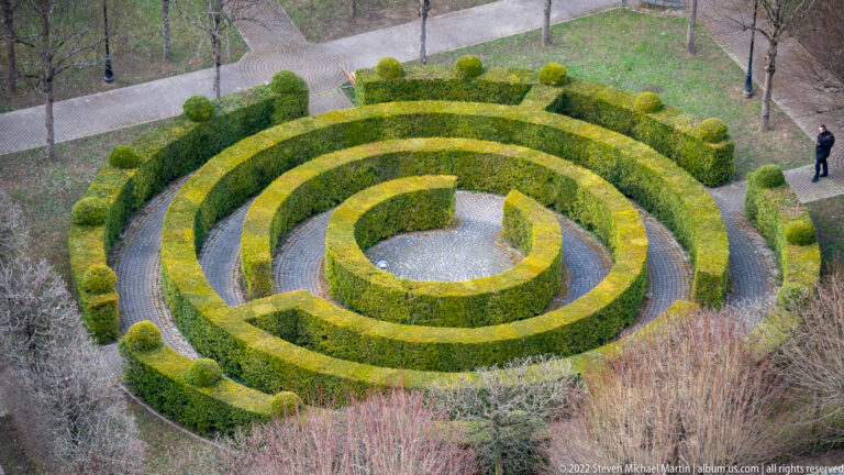 Overhead view of a circular clipped-hedge maze with concentric paths in a landscaped garden.