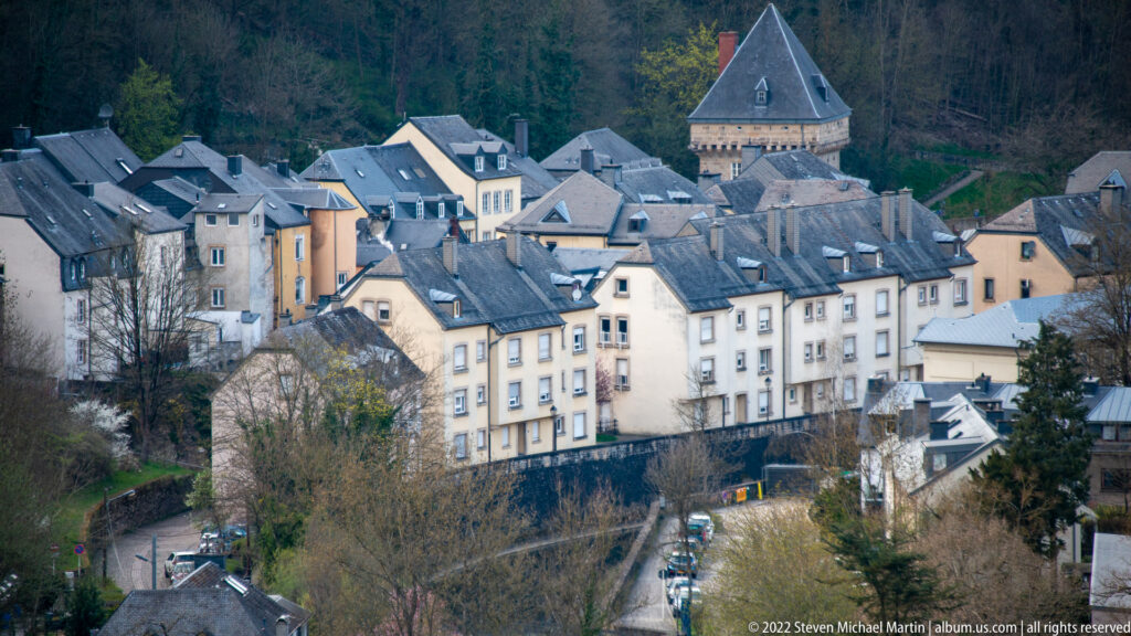 Clustered slate-roofed historic houses rise around a square stone tower on a wooded lower-city slope.