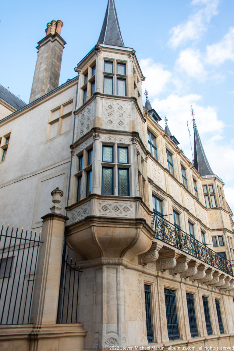 Carved polygonal oriel window projects from the Grand Ducal Palace above stone supports and ornate iron balconies.