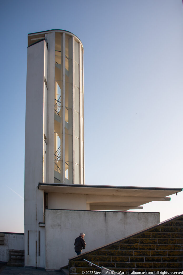 Cylindrical concrete tower beside a low flat-roofed structure, viewed against a clear blue sky.