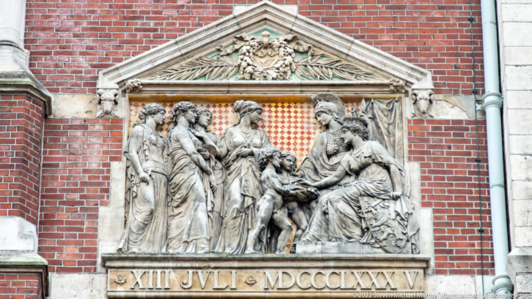 Pedimented Rijksmuseum relief with clustered carved figures above a Roman-numeral inscription.