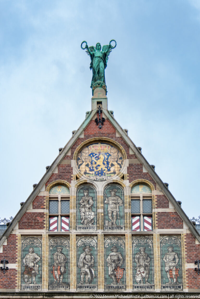 Ornate Rijksmuseum gable with painted panels, heraldic emblems, and a winged sculpture on the roof peak.
