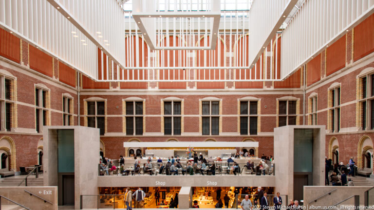Rijksmuseum Atrium with red-brick walls, white skylight structure, balconies, shops, and visitors.