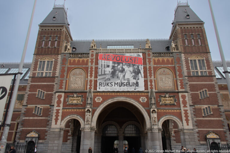 Rijksmuseum entrance between twin brick towers with a large REVOLUSI! exhibition banner above the central arch.