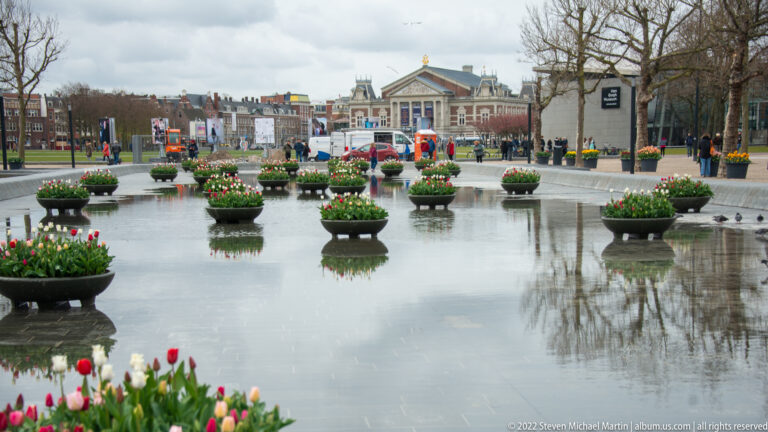 Tulip-filled circular planters in a shallow reflecting pool at Museumplein, with the Concertgebouw beyond.